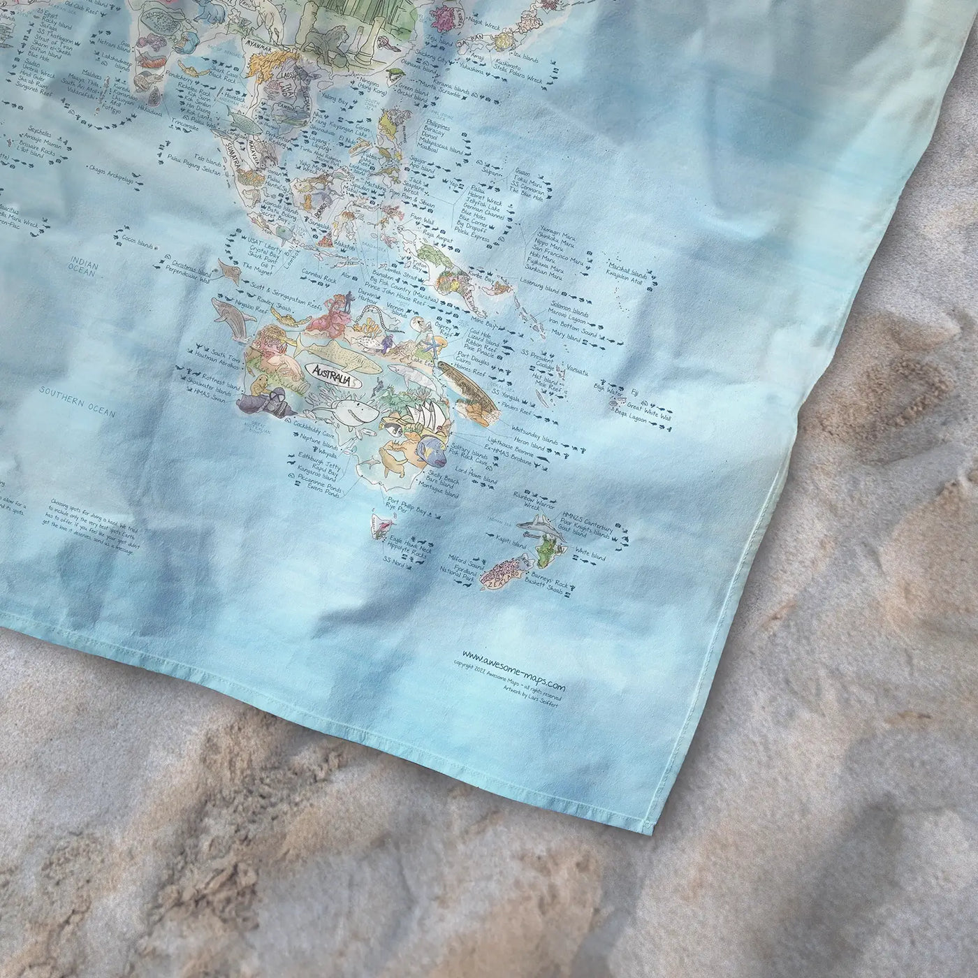 Bottom right corner of the Dive Map towel of the world lying on the sand