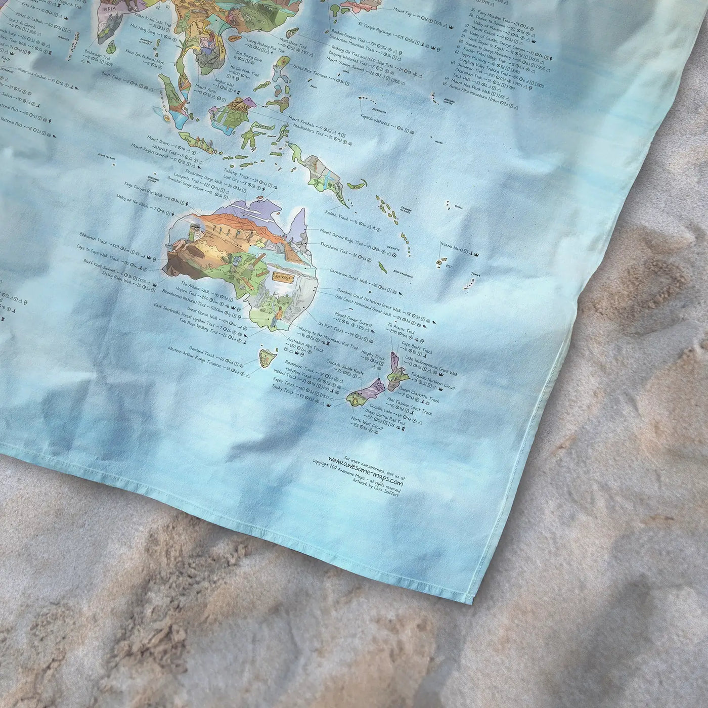 Bottom right corner of the Hiking Map towel of the world lying on the sand