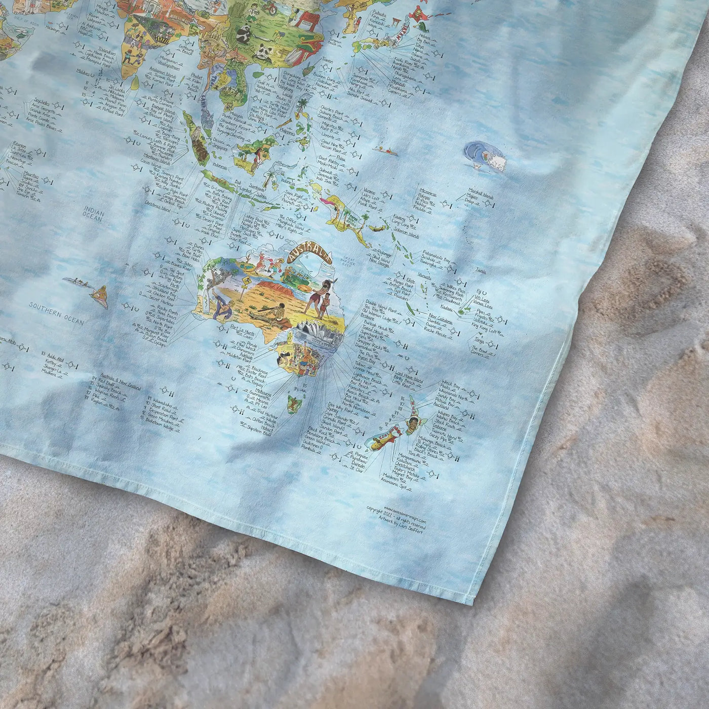 Bottom right corner of the Surftrip Map towel of the world lying on the sand.