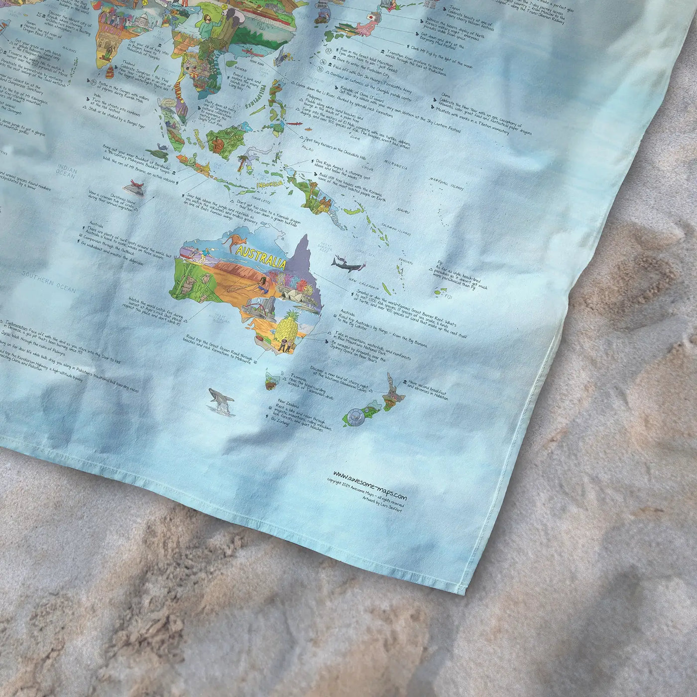 Bottom right corner of the Bucketlist Map towel of the world lying on the sand